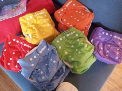 A pile of cloth nappies on a blue sofa. The nappies are brand new and in solid colours.