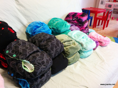 A pile of colourful and black cloth nappies on a white couch. The nappies are new. Some are smooth and some are furry.